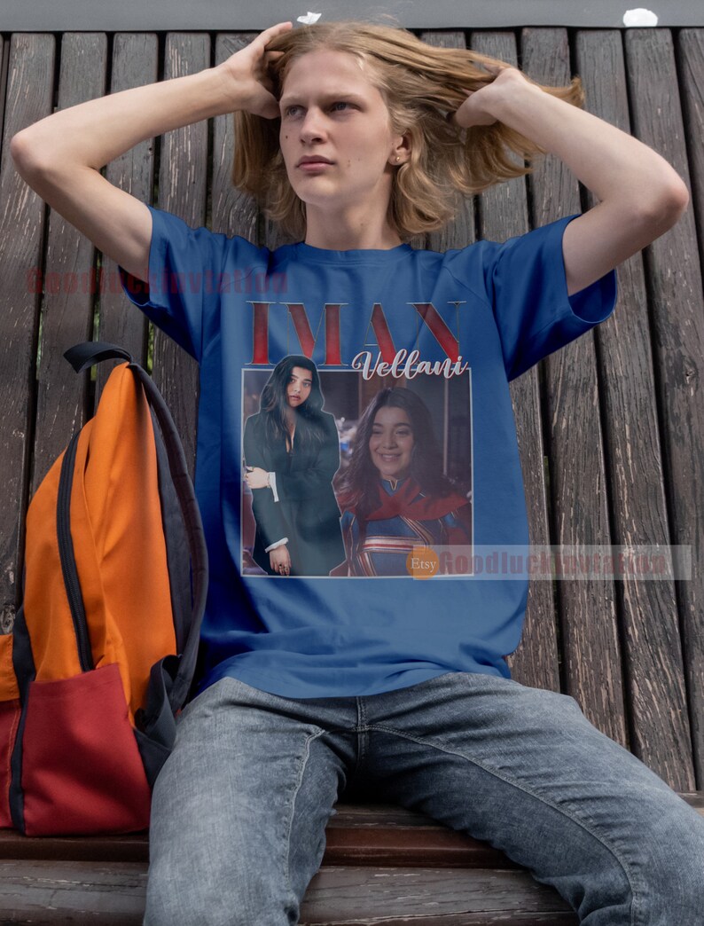 May include: A blue t-shirt featuring a photograph of a woman in a superhero costume with the text "Ms. Marvel" and "Vellani" printed on it.