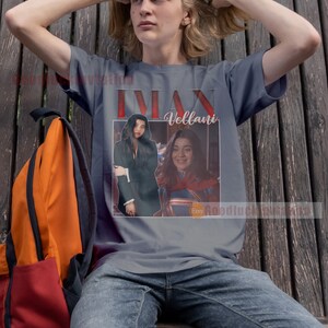 May include: A grey t-shirt featuring a graphic of a woman with long dark hair and a woman with short brown hair. The text "Iman Vellani" is printed on the shirt.