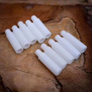 Op de afbeelding: Tien witte plastic buizen, sommige zijn op elkaar gestapeld en andere liggen plat op een houten oppervlak.