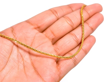 Puede incluir: Un collar de cadena de color dorado con un diseño texturizado y tejido. El collar se sostiene en la mano de una persona sobre un fondo blanco. La cadena es de un color dorado brillante y brillante.