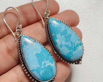 May include: A pair of teardrop-shaped earrings. Each earring features a light blue stone with a unique pattern, set in a silver-colored metal frame with a twisted rope design around the edge. The earrings have a hook closure.