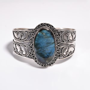 May include: Silver cuff bracelet with an oval-shaped labradorite gemstone set in a filigree design.