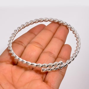 May include: A silver-colored, twisted-rope design bracelet. The bracelet is a continuous spiral, with the ends overlapping. The jewelry is shown against a neutral background.