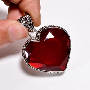 May include: A red gemstone heart pendant with a silver filigree design. The pendant is set in a silver heart-shaped frame.