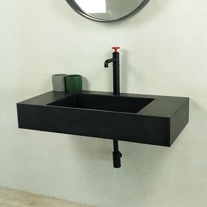May include: A black rectangular bathroom sink with a black faucet and a round mirror above it. Two small containers, one green and one grey, are on the counter.