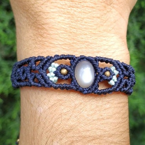 May include: A dark blue macrame bracelet with a silver oval gemstone and gold accents.