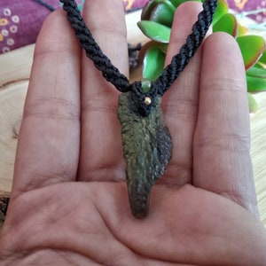 May include: A dark green stone pendant with a black cord necklace. The pendant is shaped like a jagged piece of rock.