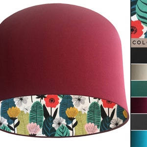 May include: A burgundy lampshade with a white floral print lining. The print features green leaves, pink, yellow, and red flowers.