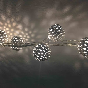 Könnte beinhalten: Eine Lichterkette mit weißen Glühbirnen in Kugelform und einem ausgeschnittenen Muster. Die Lichter sind mit einem durchsichtigen Kabel verbunden und leuchten.