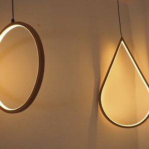May include: Two modern light fixtures hanging from the ceiling. One is a circular ring and the other is a teardrop shape.