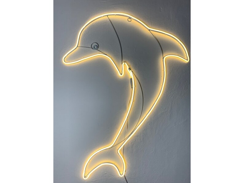 May include: A white neon dolphin sign with a yellow glow. The dolphin is jumping out of the water and has a curved tail.
