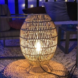 May include: A woven wicker lamp with a round, oval shape and a light bulb inside. The lamp is sitting on a woven rug.