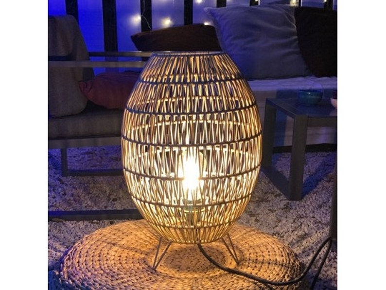 May include: A woven wicker lamp with a round, oval shape and a light bulb inside. The lamp is sitting on a woven rug.