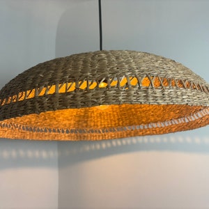 May include: A woven wicker pendant light fitting with a natural brown colour. The light fitting has a round, dome-shaped shade with a woven pattern.