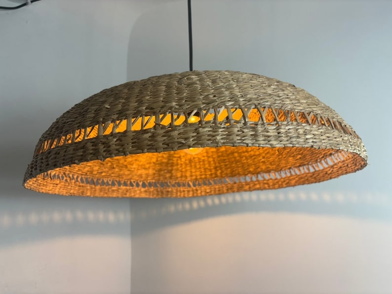 May include: A woven wicker pendant light fitting with a natural brown colour. The light fitting has a round, dome-shaped shade with a woven pattern.