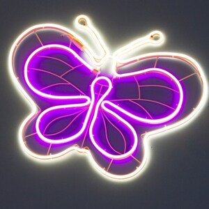 May include: A white neon butterfly with a purple outline. The butterfly is a popular design for home decor and can be used to add a touch of whimsy to any room.