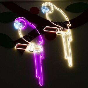 May include: Two neon parrots on a white wall. The parrot on the left is purple and the parrot on the right is white.