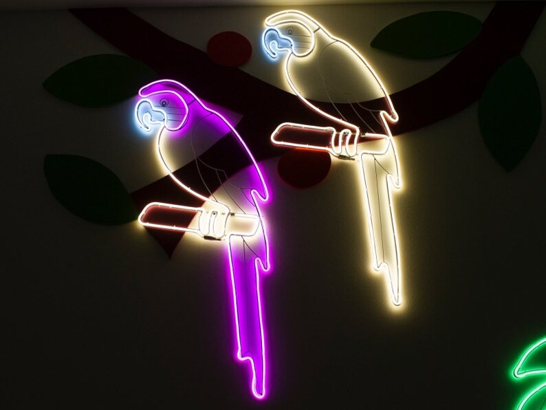 May include: Two neon parrots on a white wall. The parrot on the left is purple and the parrot on the right is white.