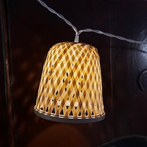 Pode incluir: Uma corda de luzes com abajures de tecido de cor castanho claro. As luzes estão penduradas num fio branco.