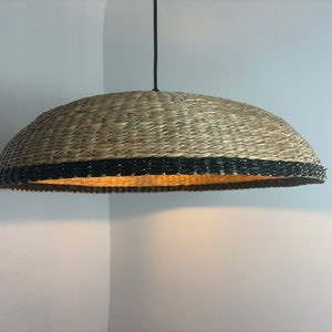 May include: A woven pendant light with a natural brown shade and a black trim. The light is hanging from a black cord.