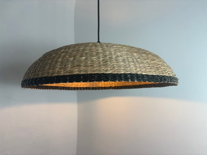May include: A woven pendant light with a natural brown shade and a black trim. The light is hanging from a black cord.