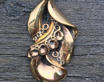 May include: A bronze pendant necklace with a detailed design of stylized leaves and berries. The pendant is attached to a silver chain.