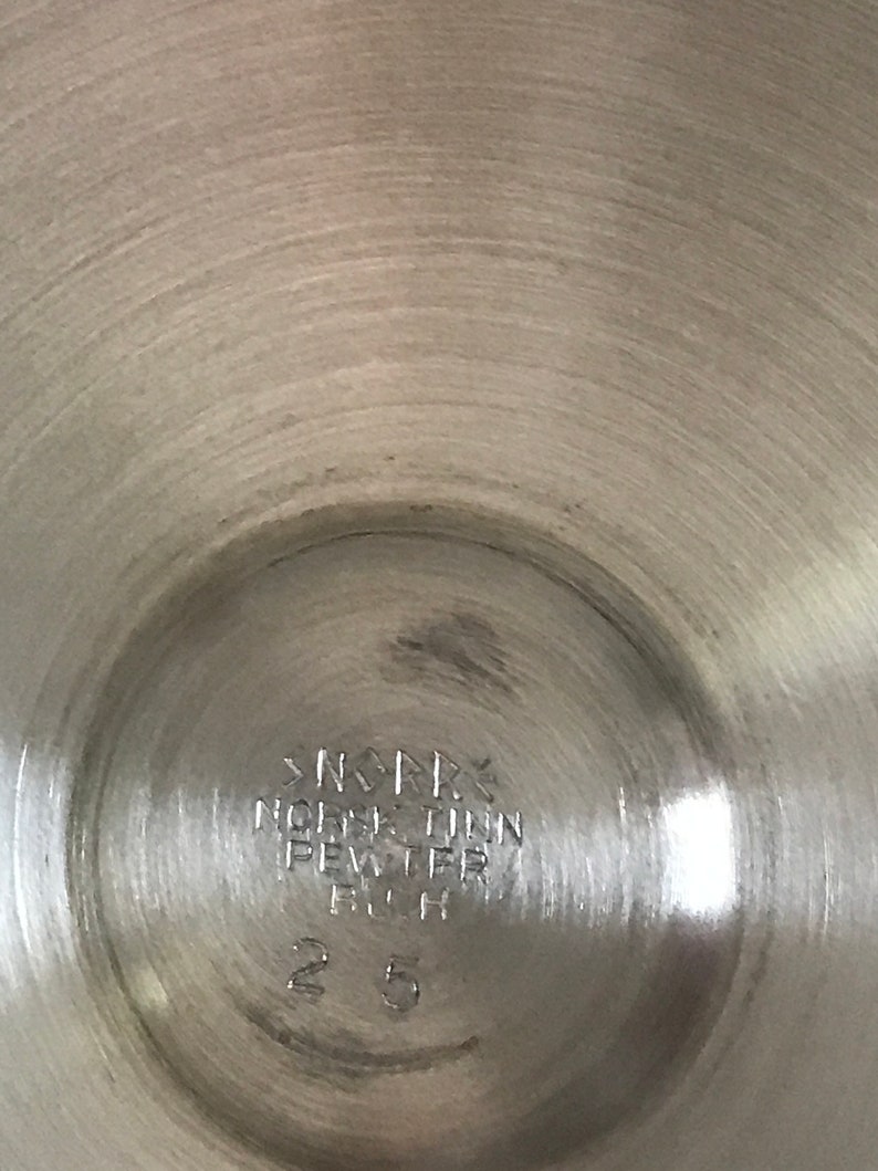 Puede incluir: Primer plano de la parte inferior de una jarra de plata con la inscripci&oacute;n "NORSK TINN PEWTER FIN 25"