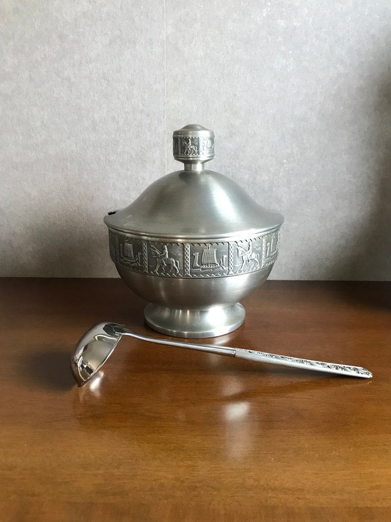 Puede incluir: Un azucarero de peltre plateado con tapa y cuchar&oacute;n a juego. El bol est&aacute; decorado con un intrincado dise&ntilde;o de figuras y animales.