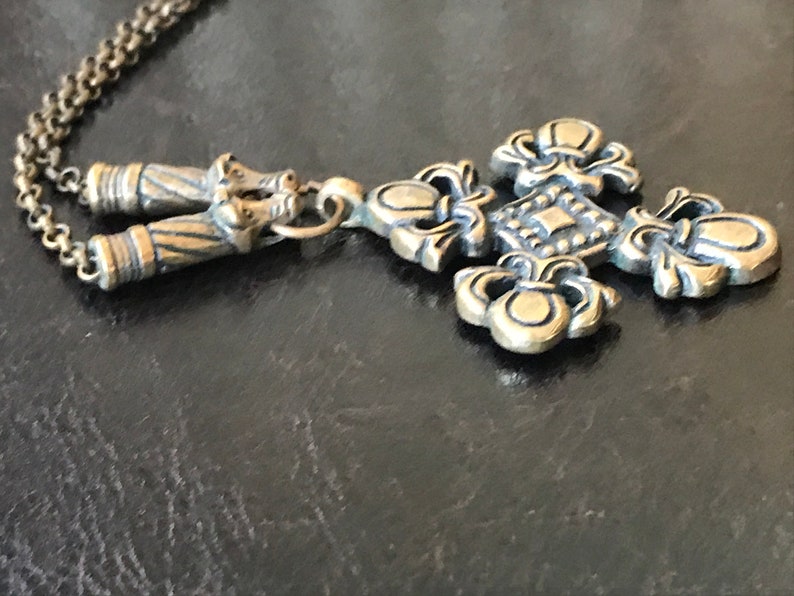 Puede incluir: Un collar dorado con un colgante de cruz adornado con detalles. La cruz tiene un centro cuadrado con un patr&oacute;n decorativo y cuatro dise&ntilde;os de flor de lis.