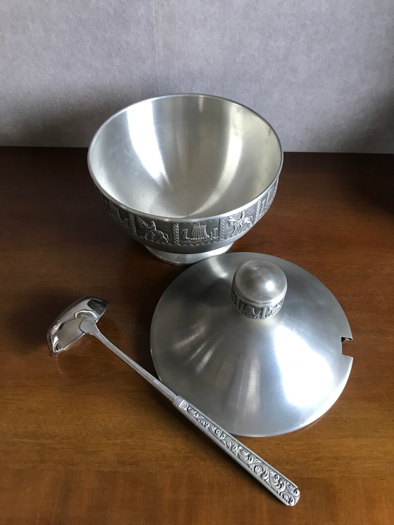 Puede incluir: Un bol de servir de plata con tapa y cuchar&oacute;n. El bol y la tapa tienen un dise&ntilde;o en relieve alrededor del borde. El cuchar&oacute;n tiene un mango decorativo.