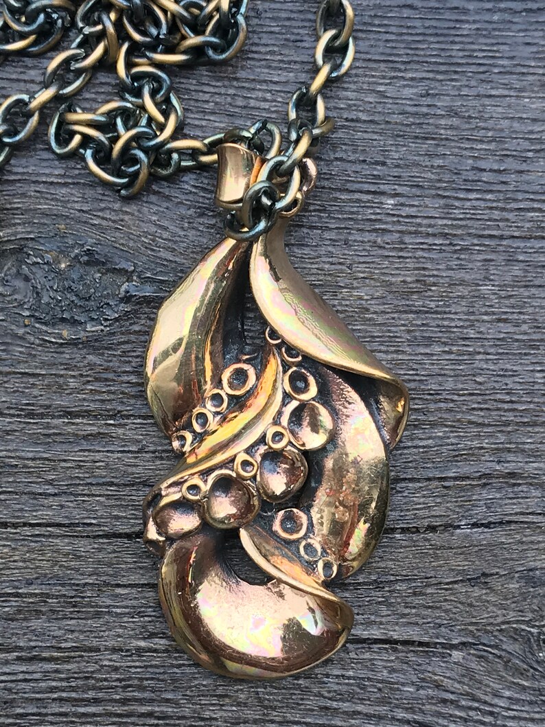 May include: A bronze pendant necklace with a detailed design of stylized leaves and berries. The pendant is attached to a silver chain.