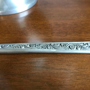Puede incluir: Un cuchillo de plata con un dise&ntilde;o floral adornado grabado en el mango.