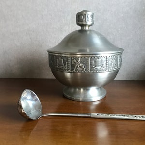 Puede incluir: Un taz&oacute;n de servir de peltre plateado con tapa y cuchar&oacute;n a juego. El taz&oacute;n tiene una banda decorativa de im&aacute;genes en relieve alrededor del borde.