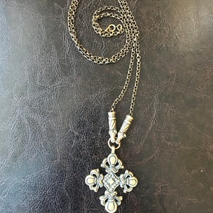 Puede incluir: Un collar de cadena dorada con un gran colgante de cruz adornado. La cruz tiene un centro en forma de diamante y detalles intrincados.