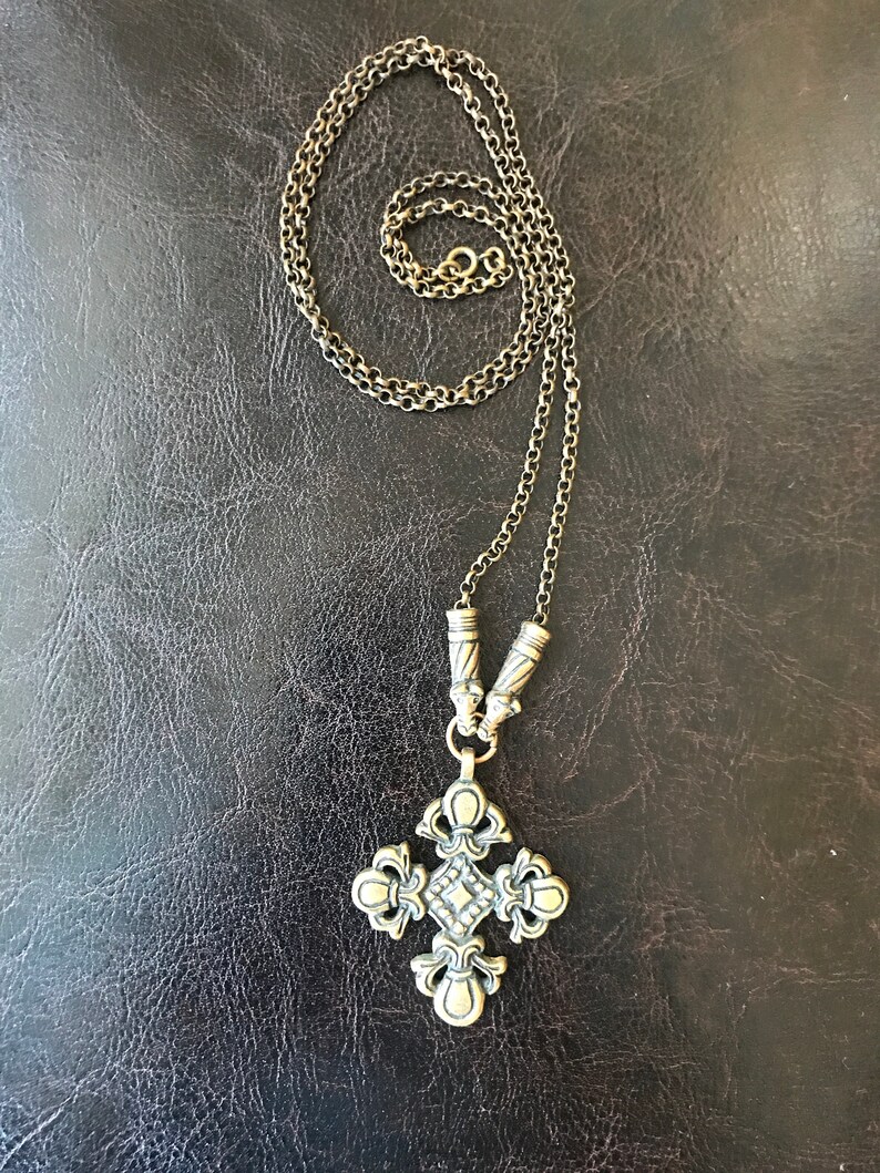 Puede incluir: Un collar de cadena dorada con un gran colgante de cruz adornado. La cruz tiene un centro en forma de diamante y detalles intrincados.