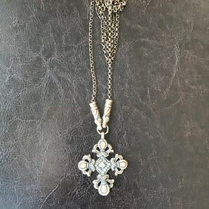 Puede incluir: Un collar de cadena de plata con un colgante de cruz de plata. La cruz tiene un dise&ntilde;o detallado con un peque&ntilde;o diamante en el centro.