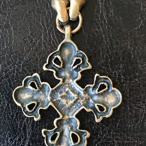 Puede incluir: Un colgante de cruz de metal dorado con detalles intrincados. La parte posterior del colgante tiene la inscripci&oacute;n "Gift from Espeland Original Made in Norway".