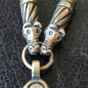 Puede incluir: Primer plano de un collar de plata con dos colgantes de cabeza de animal y un colgante decorativo en forma de tr&eacute;bol de tres hojas.