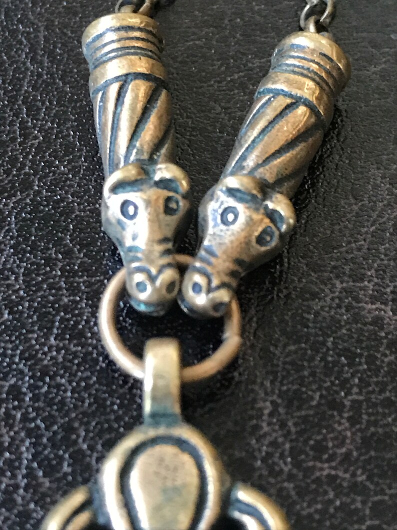 Puede incluir: Primer plano de un collar de plata con dos colgantes de cabeza de animal y un colgante decorativo en forma de tr&eacute;bol de tres hojas.