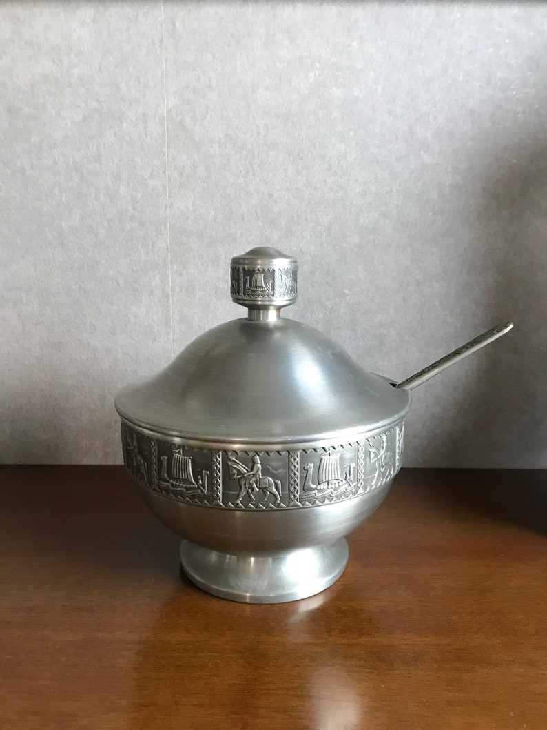 Puede incluir: Un azucarero de plata con tapa y una cucharita. El bol est&aacute; decorado con un dise&ntilde;o en relieve de barcos y caballos.