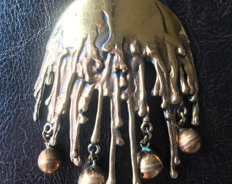 May include: A gold-toned pendant necklace with a large, abstract, textured, dripping design and five dangling round beads.