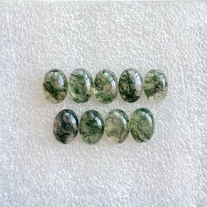 May include: Ten oval-shaped green moss agate cabochons with a white background.