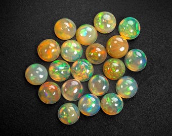 May include: A selection of spherical opals in shades of orange, green, and blue, arranged on a black background. The opals exhibit a polished, iridescent sheen, reflecting light and producing a shimmering effect. The gemstones are of varying sizes.