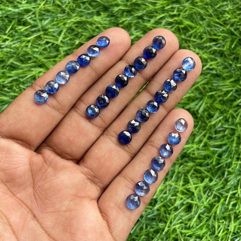 May include: A collection of 18 faceted round blue sapphire gemstones, ranging in size, displayed on a hand.