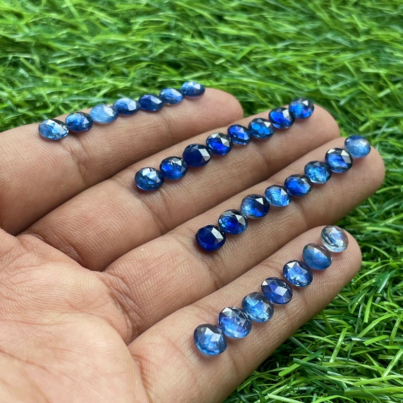 May include: A collection of round, faceted blue gemstones, likely sapphires, displayed on a hand. The gemstones are various shades of blue, ranging from light to dark.