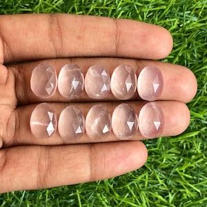 Könnte beinhalten: Acht facettierte Rosenquarzsteine, jeder mit einer hellrosa Farbe und einer glatten, polierten Oberfläche. Die Steine sind in zwei Reihen zu vier angeordnet, wobei die obere Reihe leicht versetzt zur unteren Reihe ist.