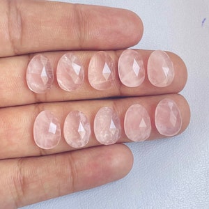 Könnte beinhalten: Zehn facettierte Rosenquarzsteine in verschiedenen Rosatönen. Die Steine sind oval geformt und haben eine glatte, polierte Oberfläche.