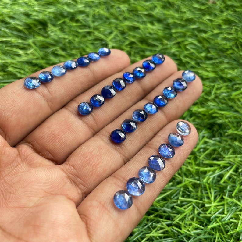 May include: A collection of 20 round, faceted, blue sapphire gemstones. The gemstones are arranged in rows on a hand, with the largest gemstones at the top and the smallest gemstones at the bottom.
