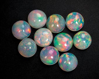 May include: Ten spherical opals with a shimmering play of colour, including green, orange, and blue, are displayed against a black backdrop. The opals' iridescent qualities are emphasized by the dark background, showcasing their round form.