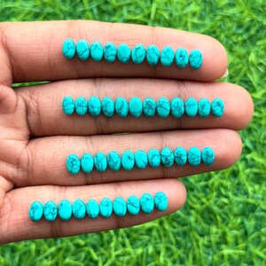 Peut inclure: Rangées de pierres précieuses ovales en turquoise avec des veines bleu foncé. Les pierres sont d'un bleu-vert vif et vibrant. Les pierres sont présentées sur une main, avec un fond vert.
